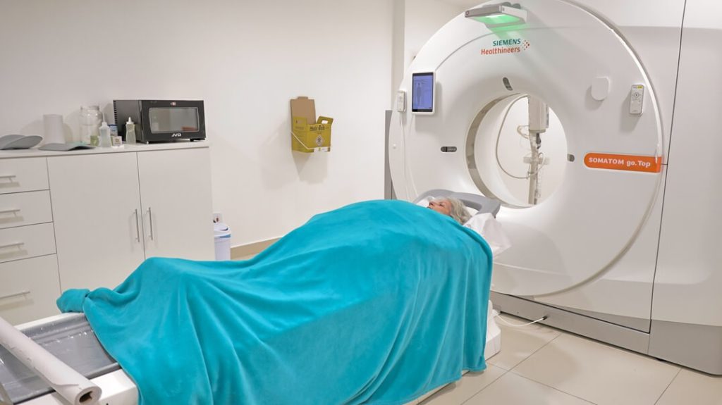 Pessoa deitada na mesa do tomógrafo em sala onde é realizada a angiotomografia coronariana na Lagos Scan, Araruama