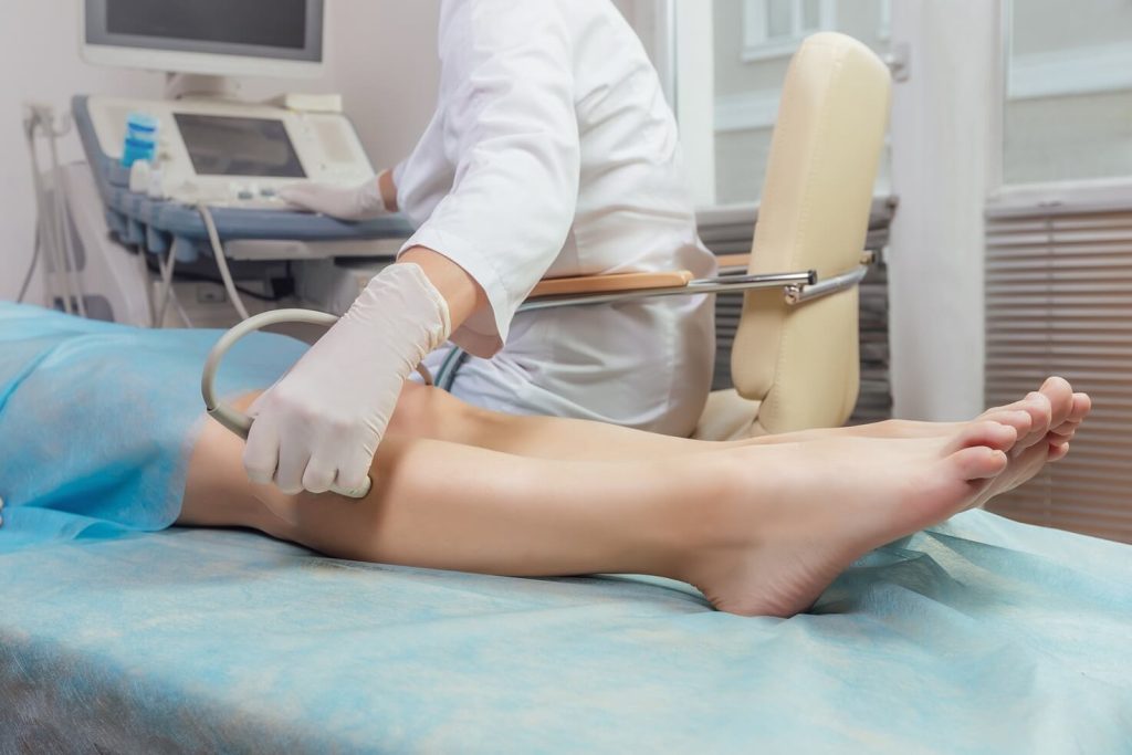 Profissional de saúde realizando exame de ultrassom com Doppler venoso nos membros inferiores de um paciente na clínica Lagos Scan, em Araruama.