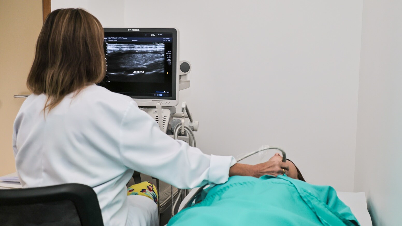 Drª Margareth Catharino, médica radiologista, realizando exame de ultrassom na região do pescoço de uma paciente deitada na maca da clínica Lagos Scan, em Araruama.
