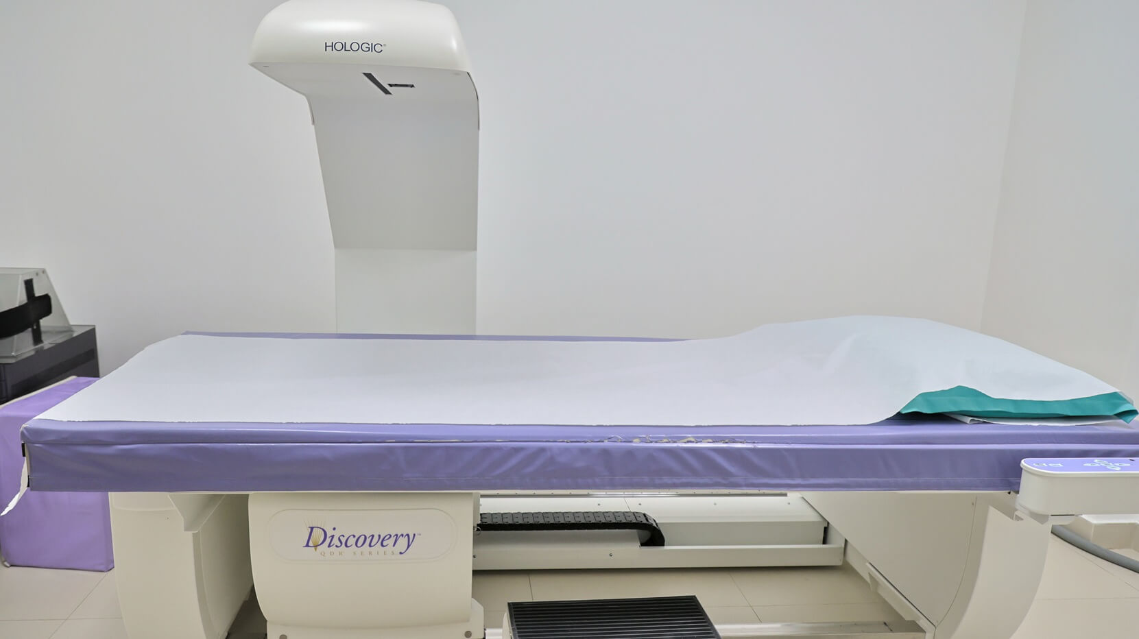 Aparelho de densitometria óssea Discovery com mesa aberta e braço digitalizado na sala de exames da Lagos Scan, em Araruama