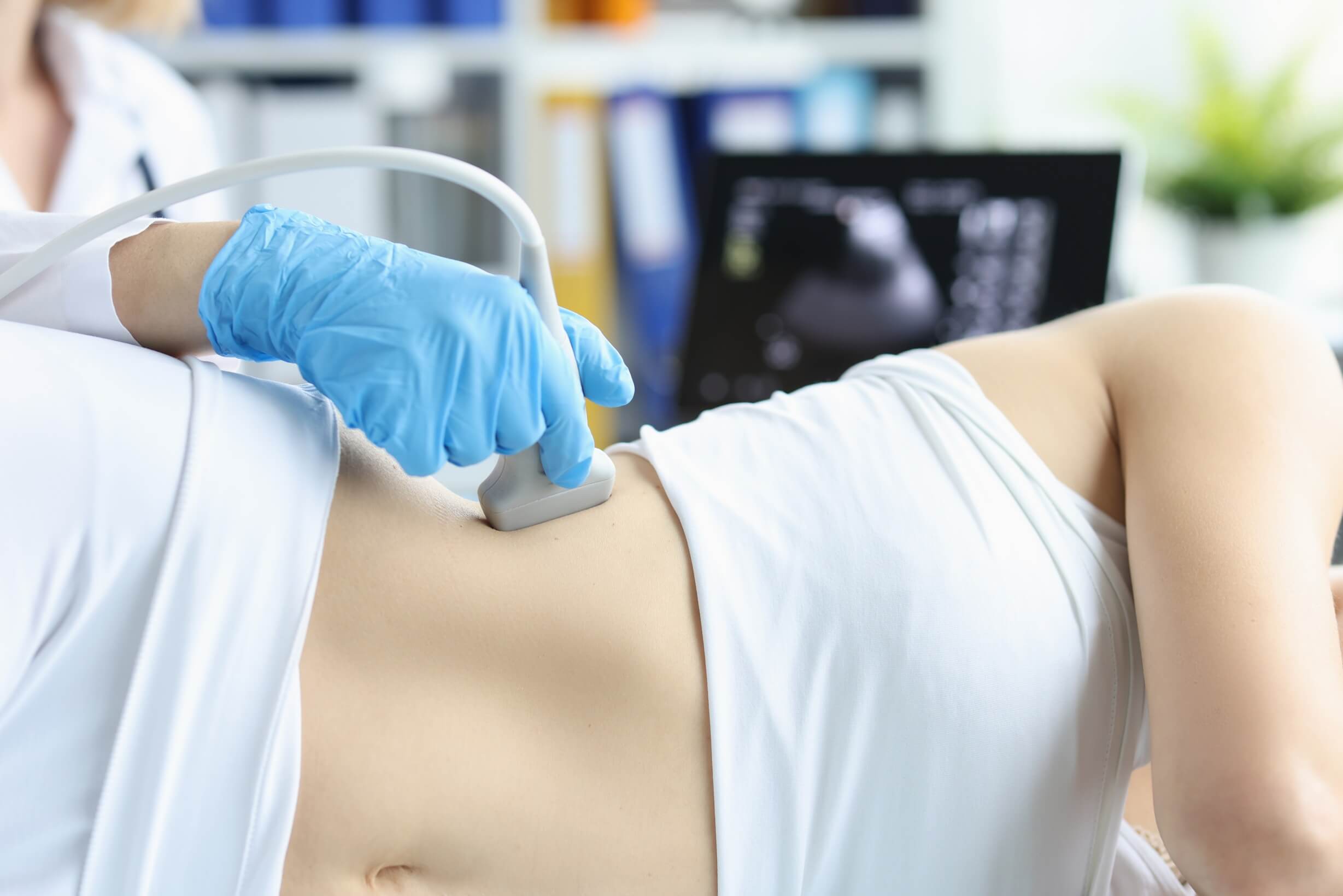 Médico realizando exame de ultrassonografia renal com transdutor posicionado no flanco da paciente para investigar cálculo nos rins.